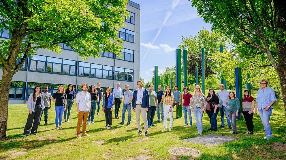 Eine Gruppe von Mitarbeitenden steht auf der Wiese vor einem Unigebäude
